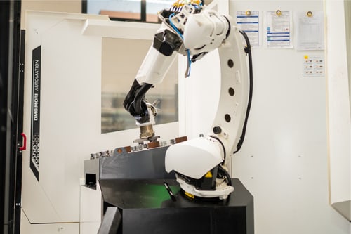 Weißer Roboterarm legt ein Bauteil in eine CNC-Maschine ein